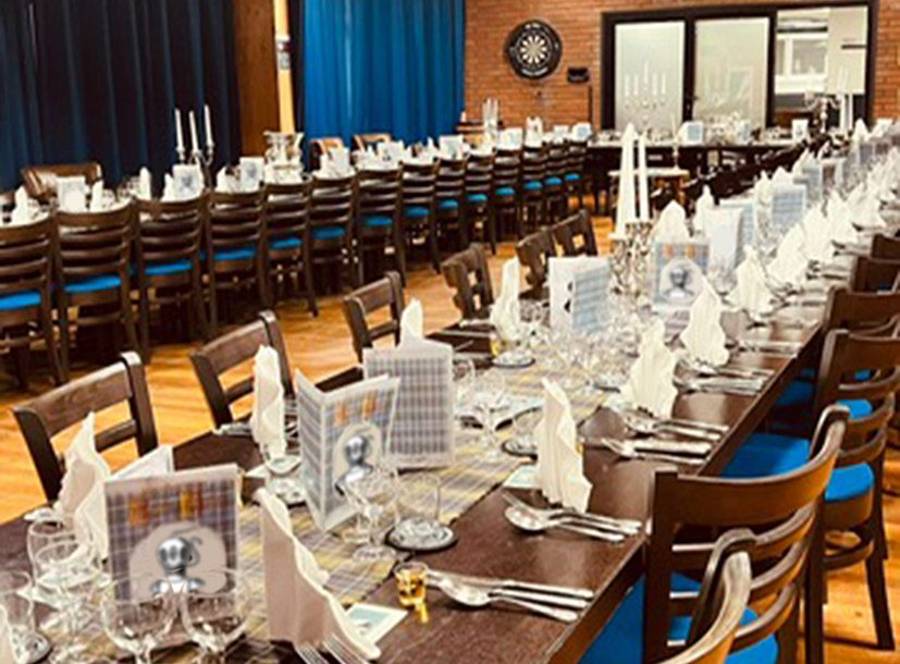 View of a dining room: two long tables dressed with silverware and candelabra for an evening dinner
